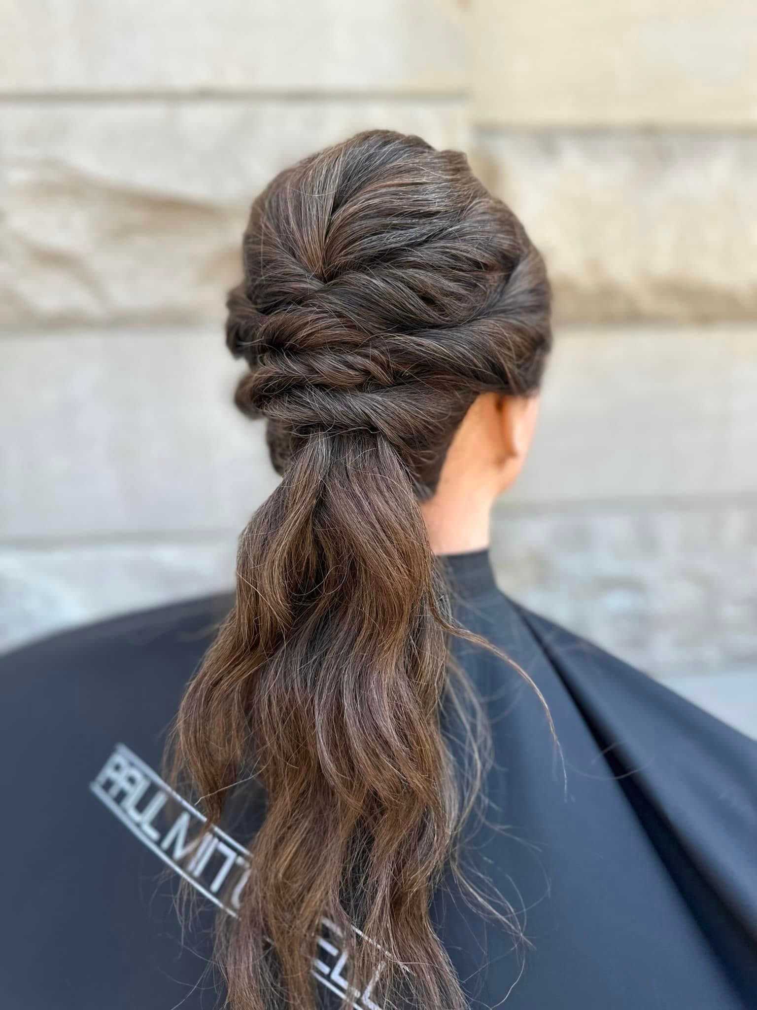 Elegant twisted and braided updo on dark brown hair, displayed against a gray stone background.