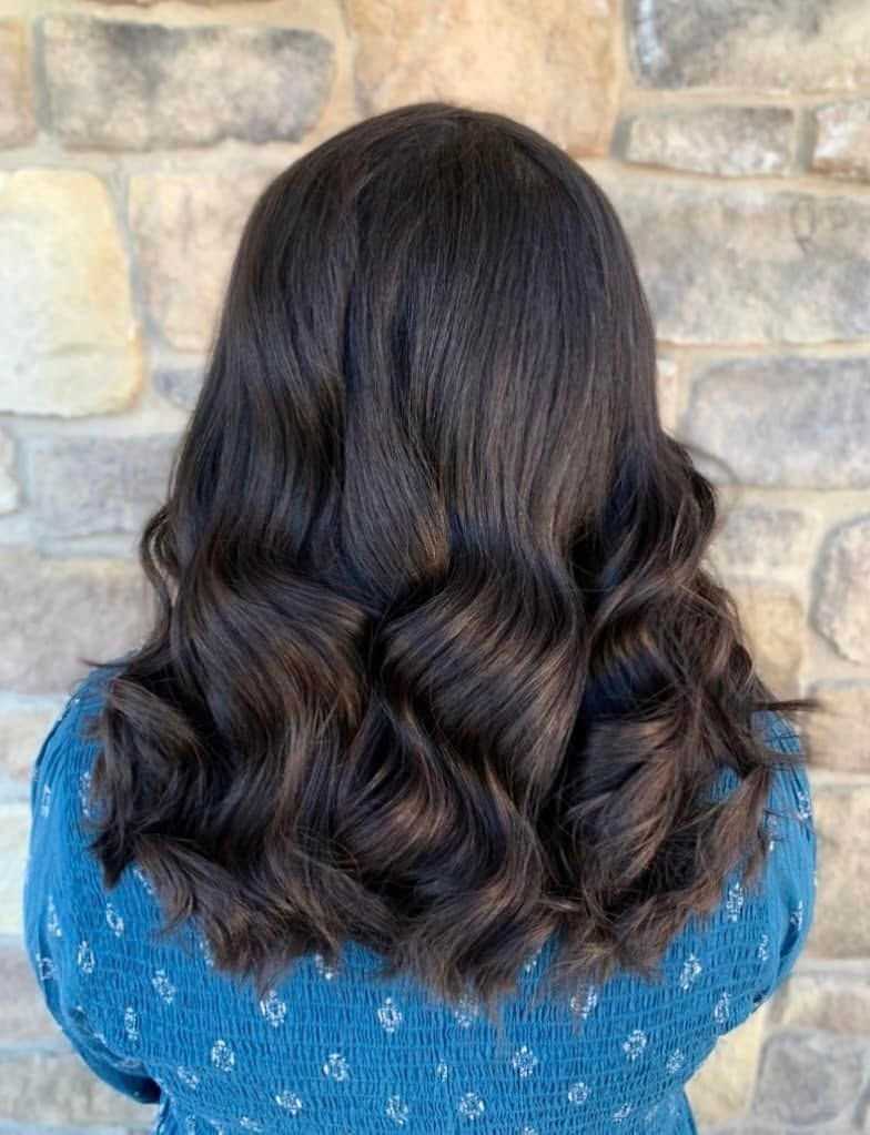 Person with dark wavy hair facing a stone wall.