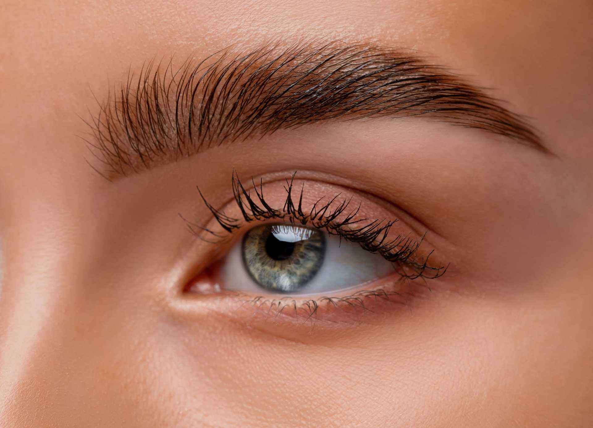 Close-up of a well-groomed eyebrow and green eye, highlighting detailed makeup and natural beauty.