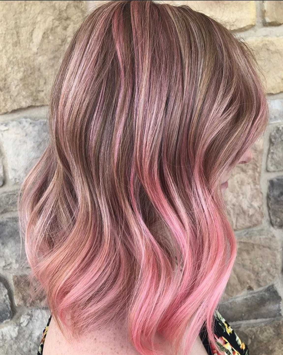 Wavy pink ombre hairstyle against a stone wall background.