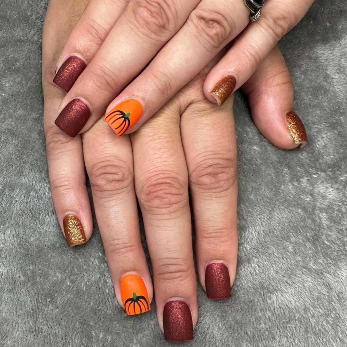 Festive autumn-themed manicure with pumpkin nail art on orange and gold accent nails.