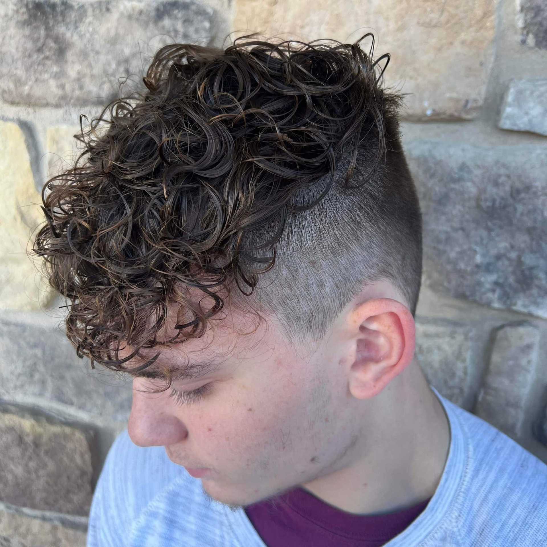 Man with curly hair and undercut hairstyle against a stone wall background.