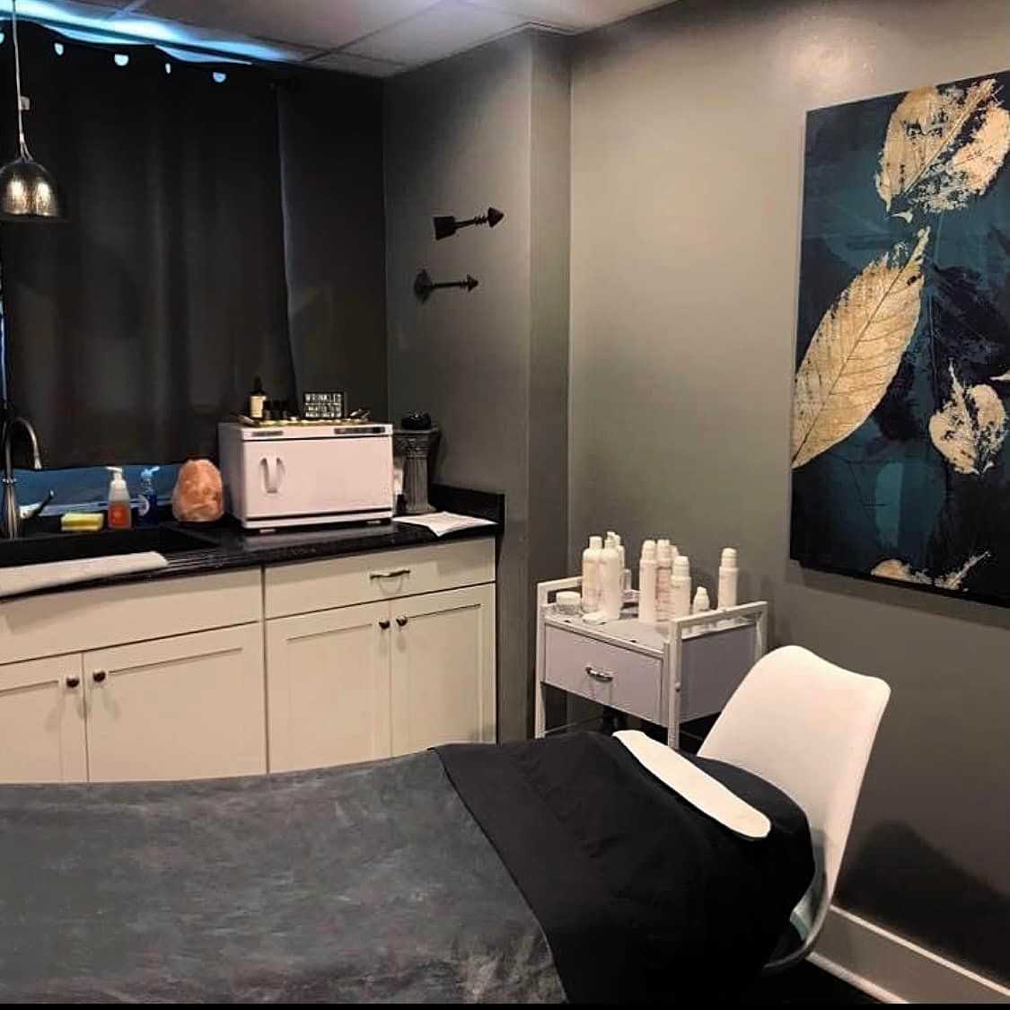 Spa treatment room with a bed, wall art, skincare products, and a soothing ambiance.