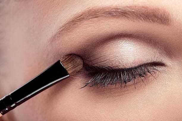 Close-up of an eye with makeup brush applying eyeshadow on the eyelid.