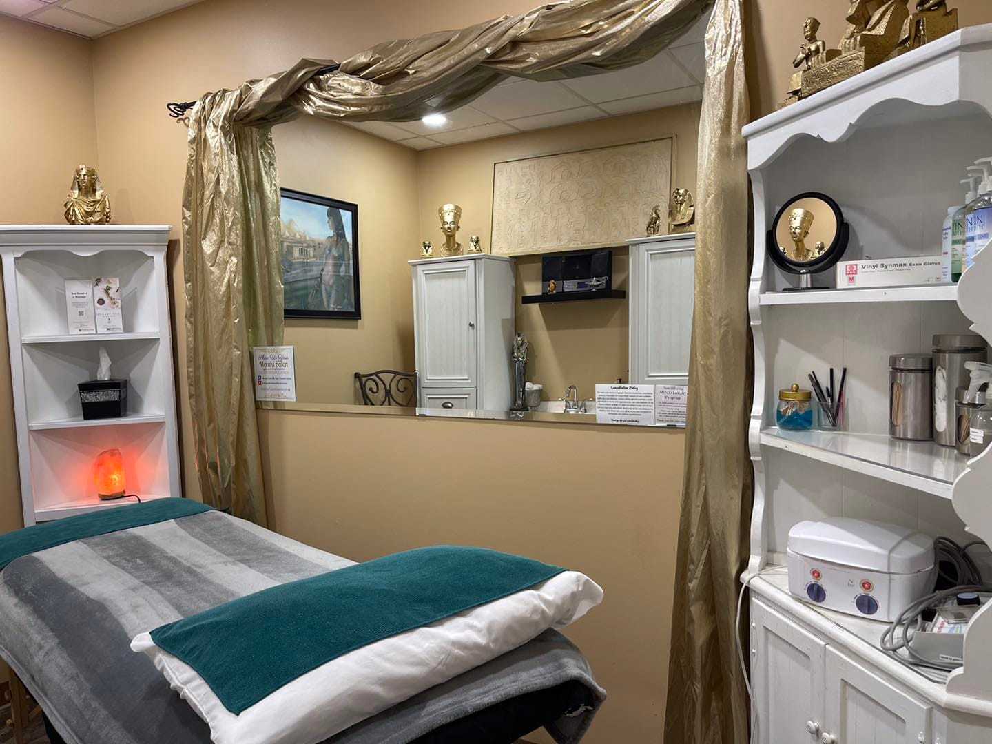 Massage therapy room with a neatly made bed, decorative shelves, and a calming ambiance.